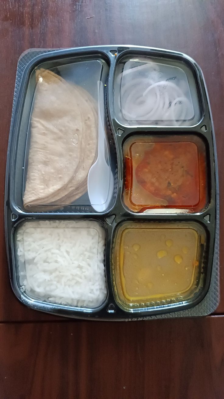 a metal tray filled with food on top of a wooden table next to a spoon