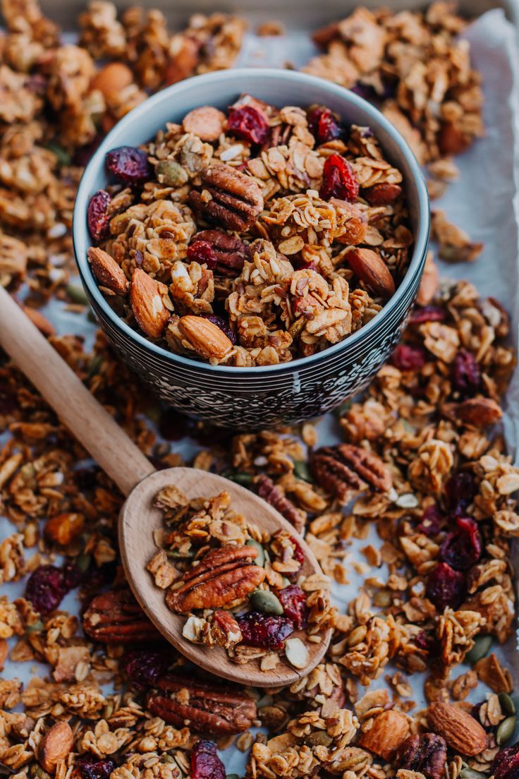 granola with nuts and cranberries in a bowl next to a wooden spoon