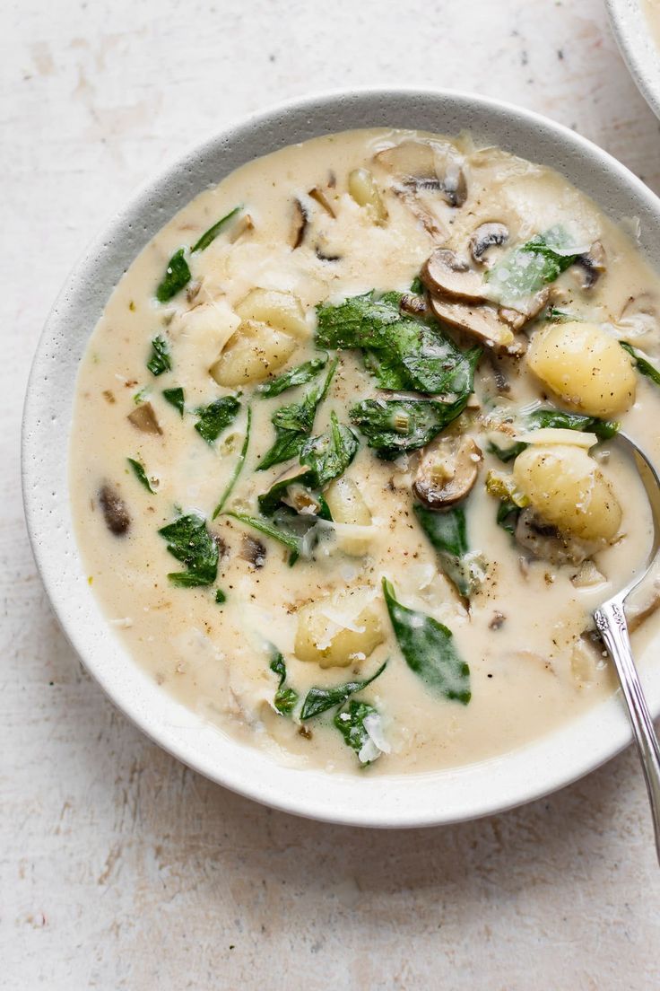 a bowl of soup with spinach, potatoes and mushrooms on the side next to a spoon