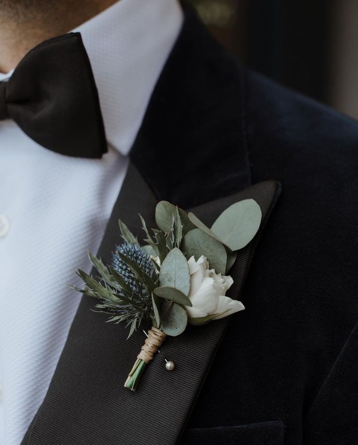 a man in a tuxedo wearing a boutonniere with white flowers and greenery