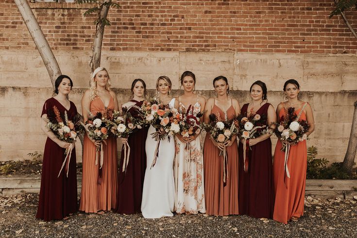 a group of women standing next to each other in front of a brick wall holding bouquets