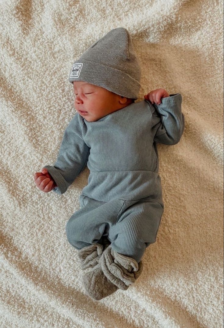 a baby laying on top of a bed wearing a gray knitted outfit and hat