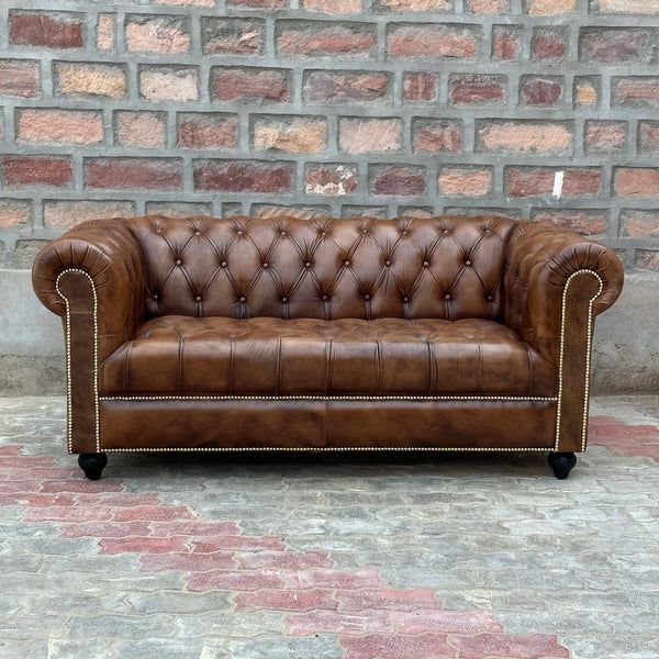 a brown leather couch sitting on top of a brick floor next to a stone wall