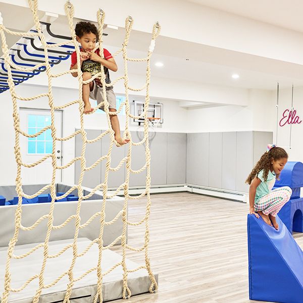 two children are playing in an indoor play area with ropes and climbing equipment on the floor