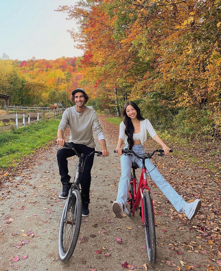 A couple is smiling at the camera as they are riding bikes past trees with orange and yellow leaves. They are enjoying the perfect fall date idea. Couples Riding Bikes, City Date Ideas, Active Couple Aesthetic, Couple Activities Photos, Biking Date, October Date Ideas, Bike Ride Date, Couple Bike Ride, Active Date Ideas