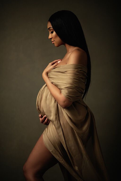 a pregnant woman in a tan dress poses for a photo with her hands on her belly