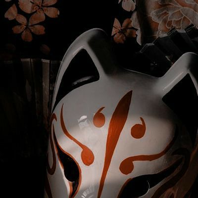 a close up of a white mask with orange designs on it's face and black background