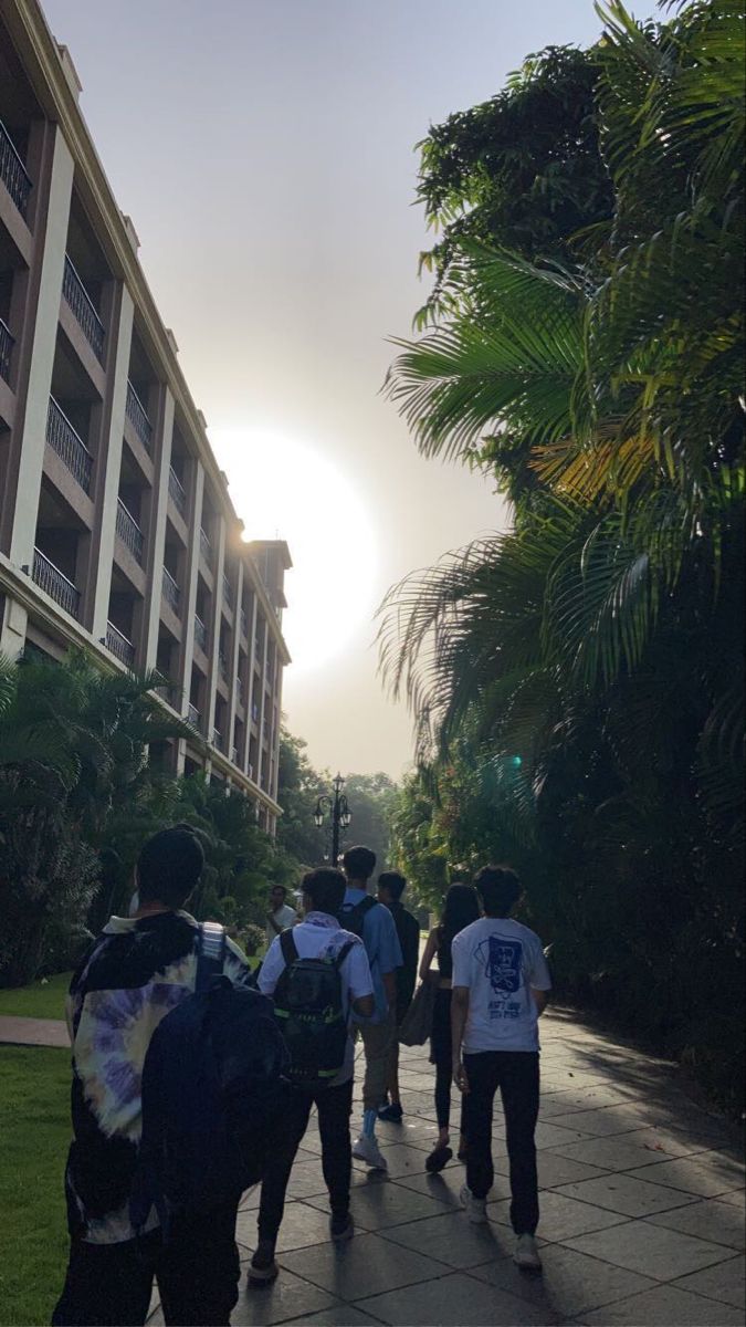 several people are walking down the sidewalk in front of an apartment building with palm trees