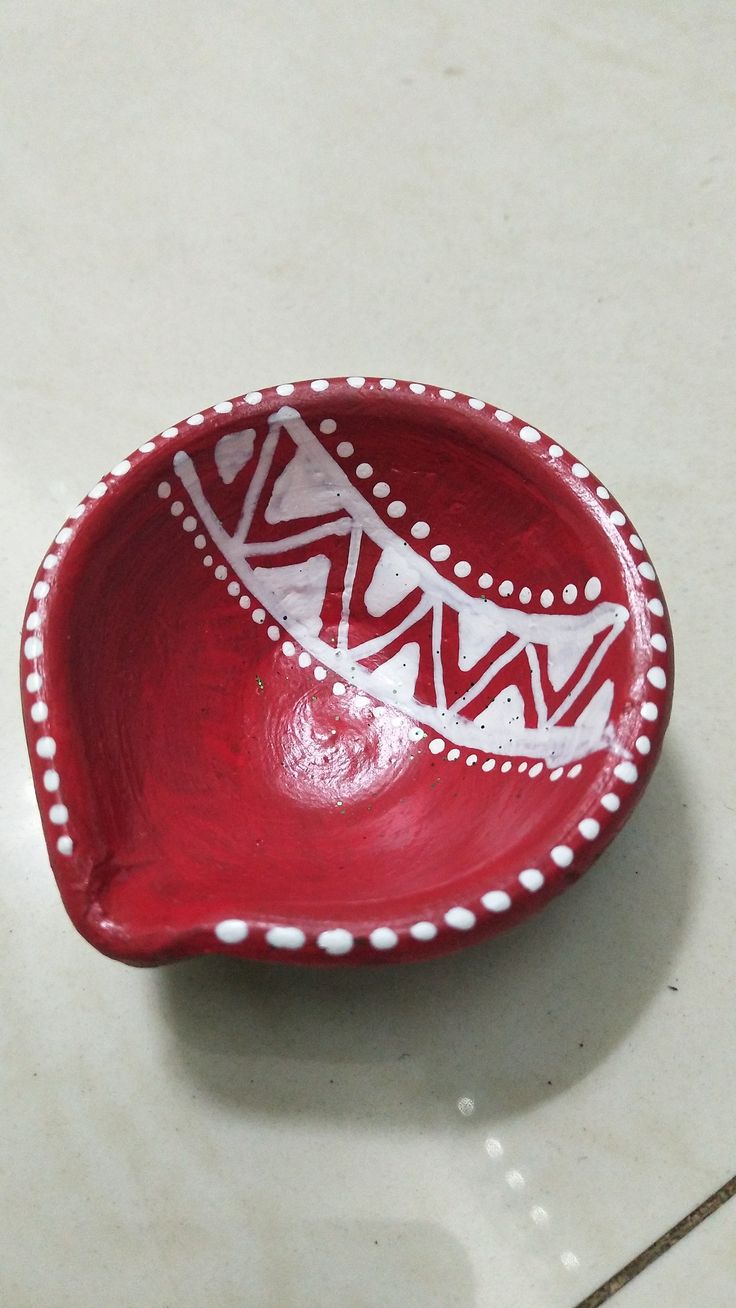 a small red bowl with white designs on the rim and bottom, sitting on a tile floor