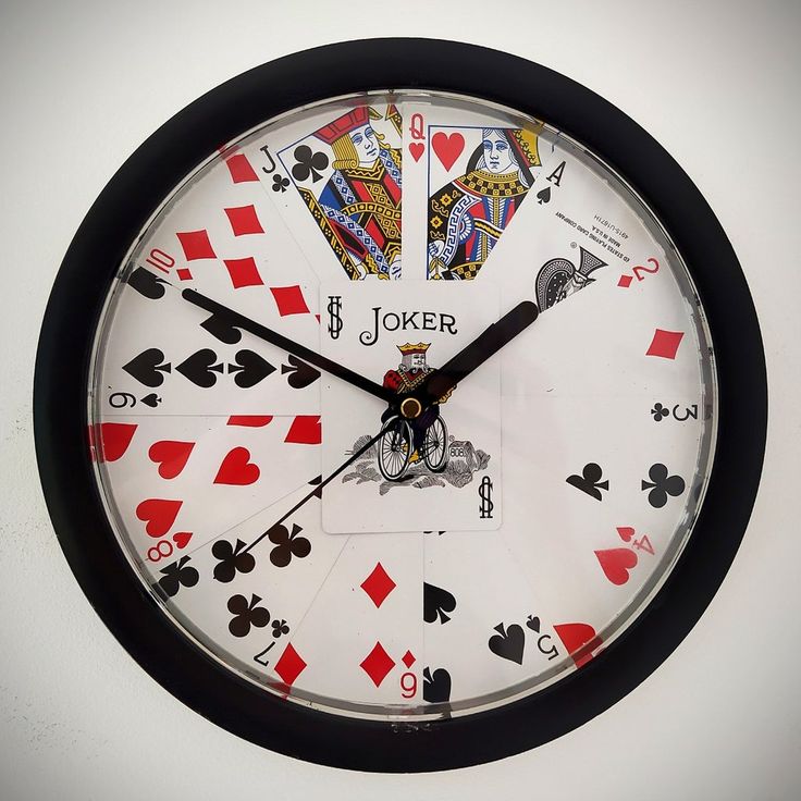 a clock with playing cards on it is hanging from the wall in front of a white wall