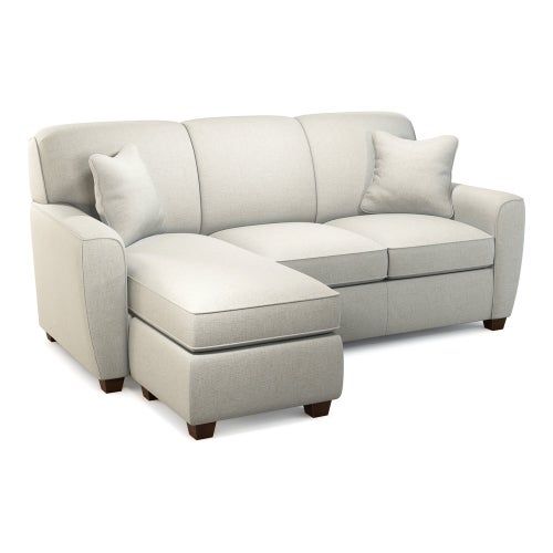 a white sectional couch with pillows on the back and foot rest in front of it