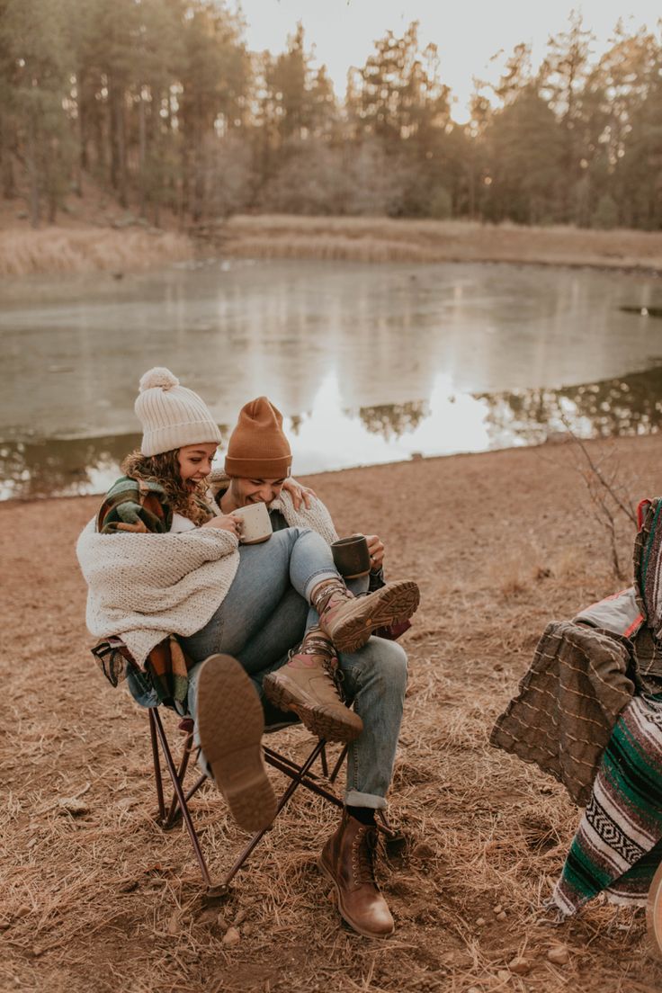 two people sitting in camping chairs next to a lake