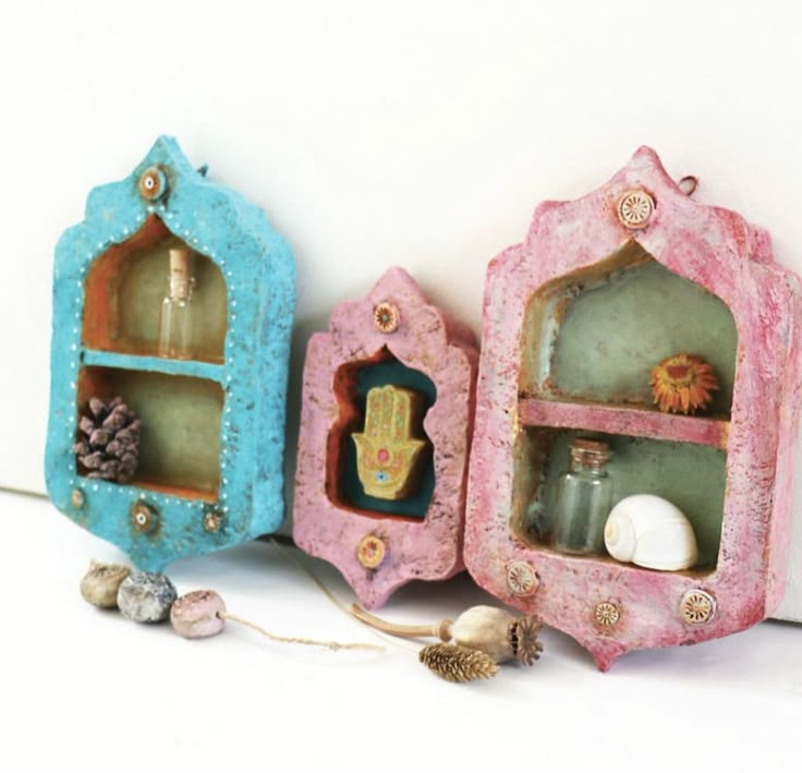 three miniature shelves with decorative items in them on a white surface, one is painted pink and the other is blue