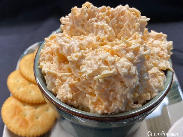 a bowl full of chicken salad next to crackers on a plate with blue cloth