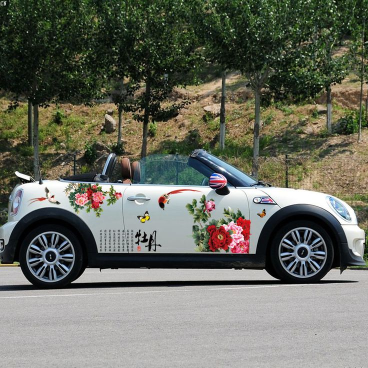 a white car with flowers painted on it's side driving down the road in front of some trees