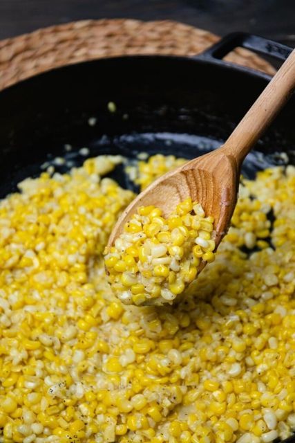 a wooden spoon scooping corn out of a skillet