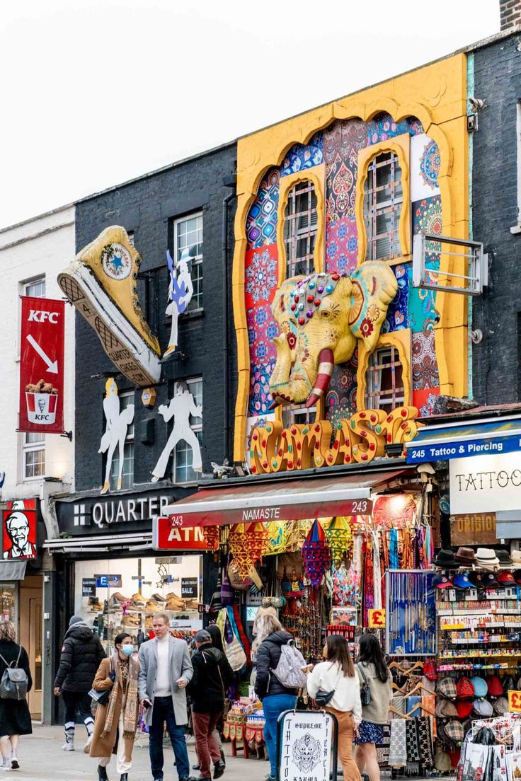 many people are walking on the sidewalk in front of some shops and stores that have been decorated with colorful designs