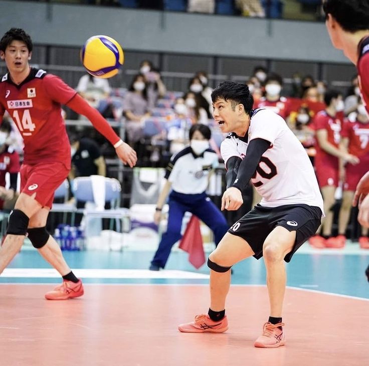 a group of young men playing a game of volleyball on an indoor court with people watching