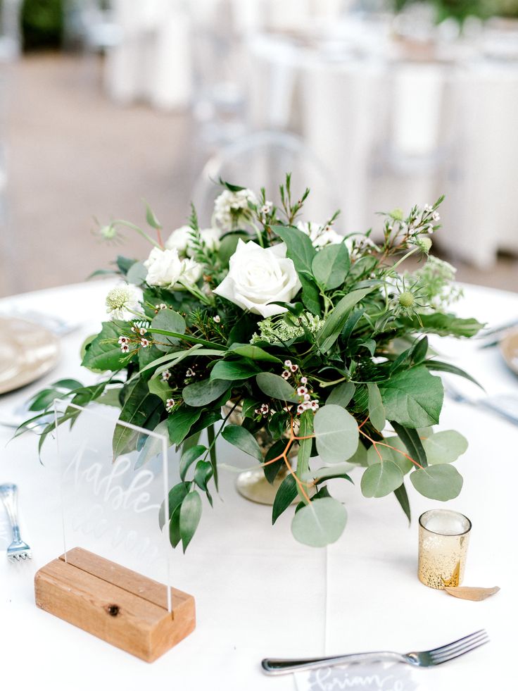 the centerpieces on this table are white roses and greenery, along with silverware