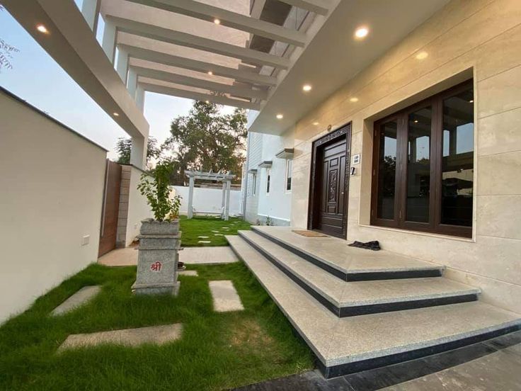 an outdoor area with grass and steps leading up to the front door is lit by recessed lights