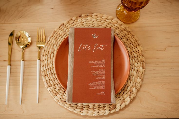 a place setting with an orange menu and silverware