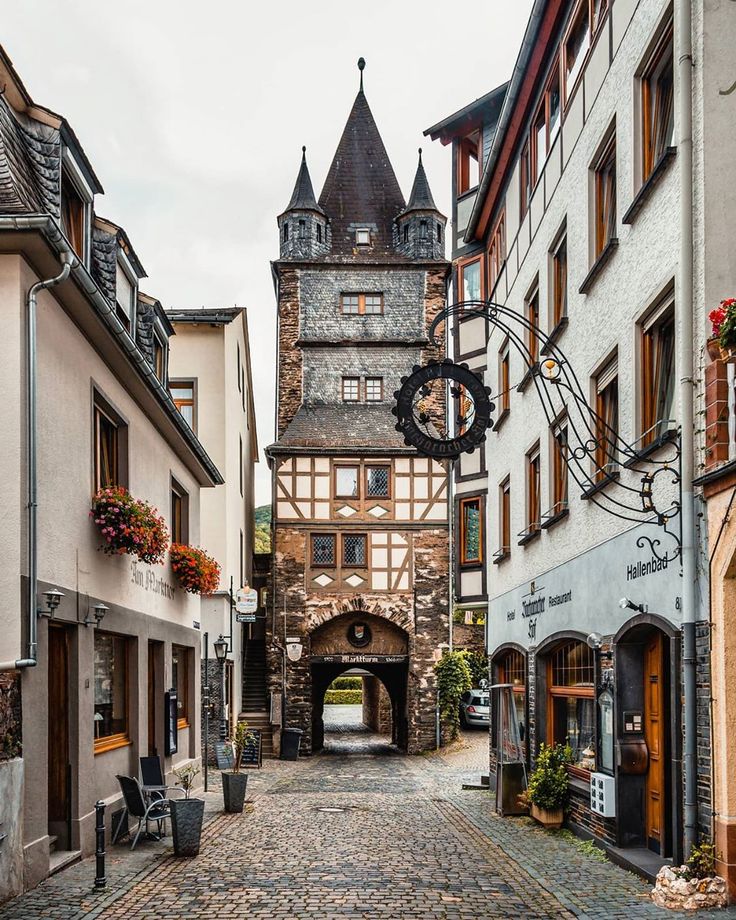 a cobblestone street lined with buildings and an arch in the middle that leads to a clock tower