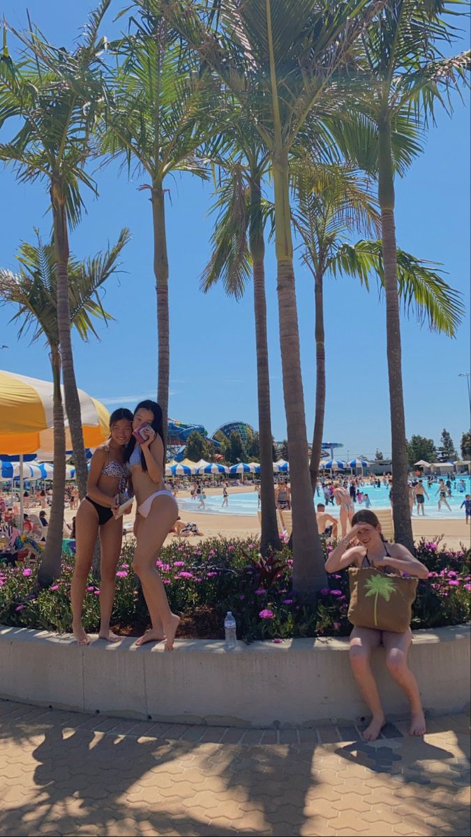 two women in bikinis standing on the edge of a wall next to palm trees