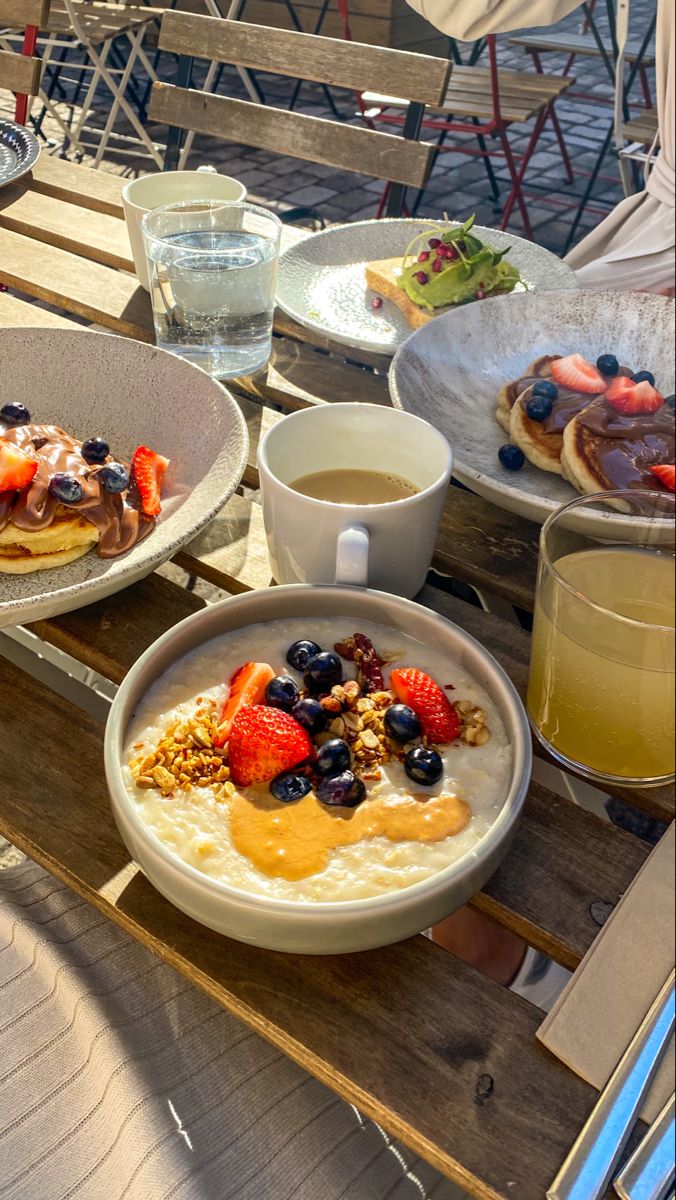 a table topped with plates of food next to cups of coffee and water on top of it