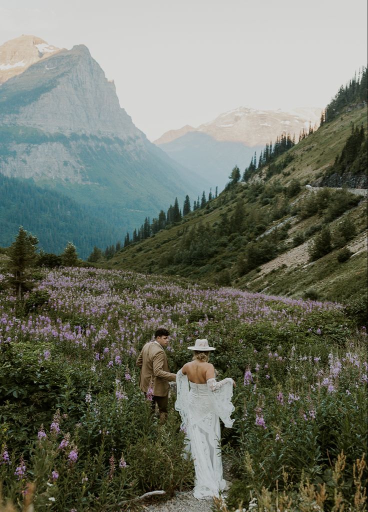 a bride and groom are walking through the wildflowers at their wedding in the mountains