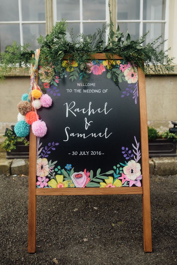 a chalkboard sign decorated with pom poms and greenery for a wedding