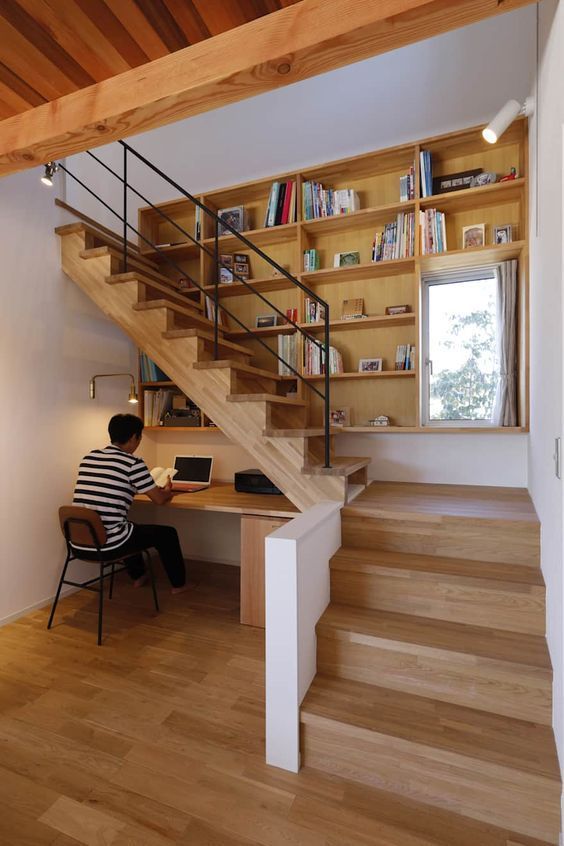 a person sitting at a desk in front of a book shelf under a stair case