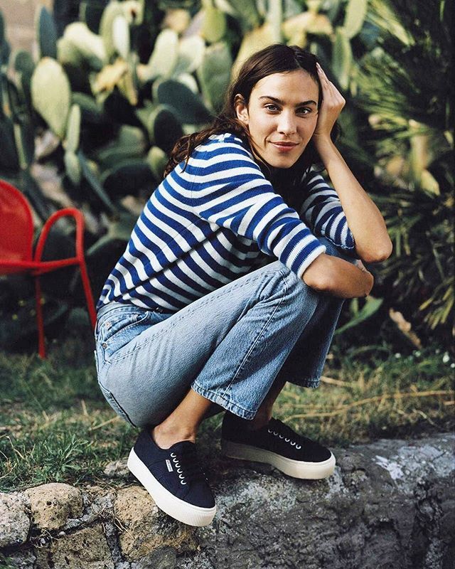 a young woman sitting on top of a rock next to a red chair and cacti