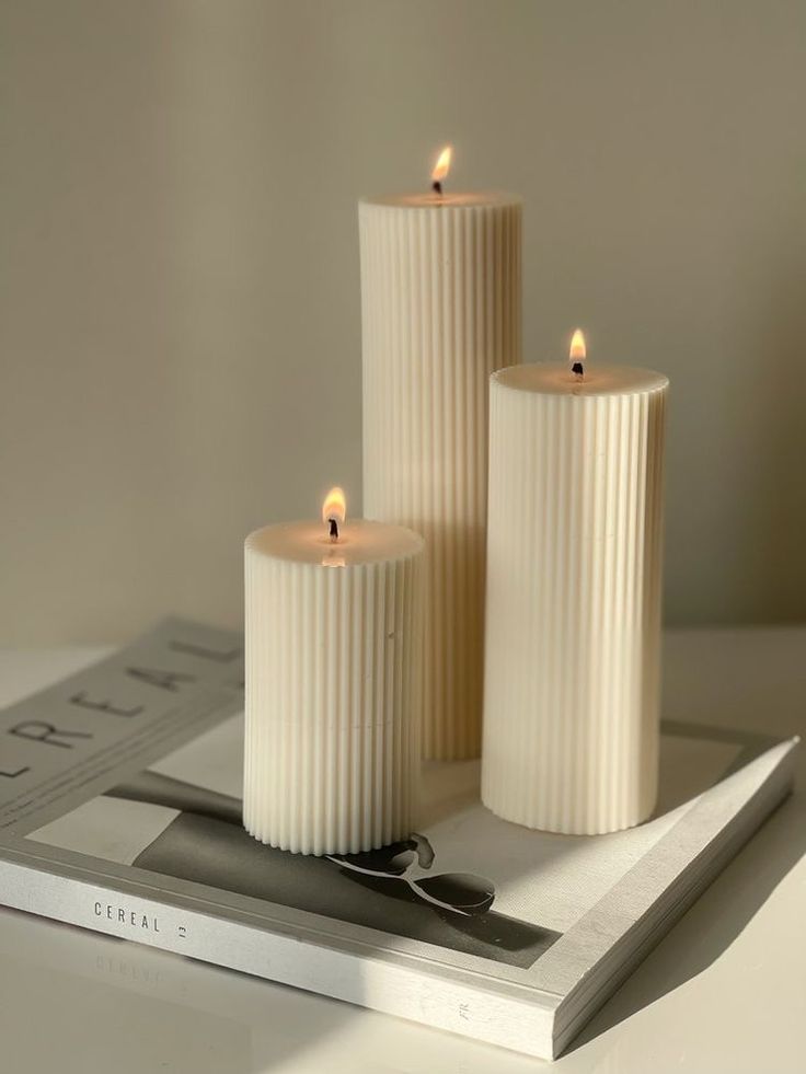 three white candles sitting on top of a book