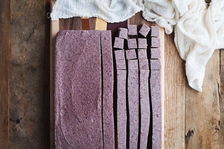 a wooden cutting board topped with slices of purple cake next to a white dish towel