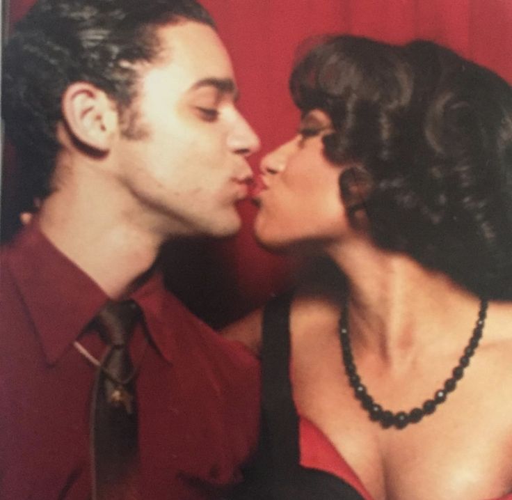 a man and woman kissing each other in front of a red curtain