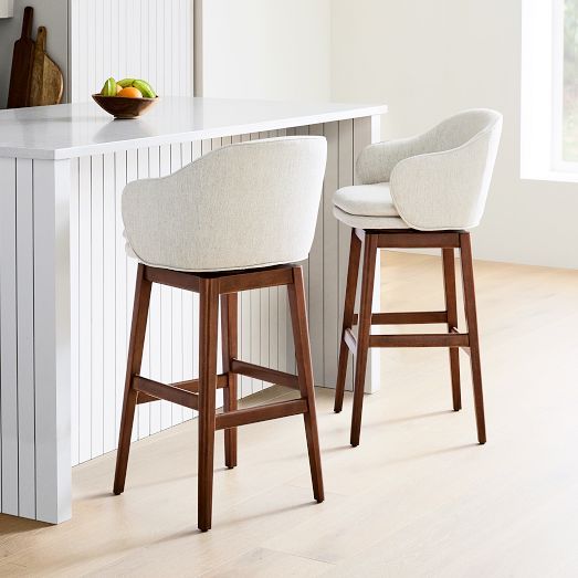 two white bar stools sitting in front of a counter top with fruit on it