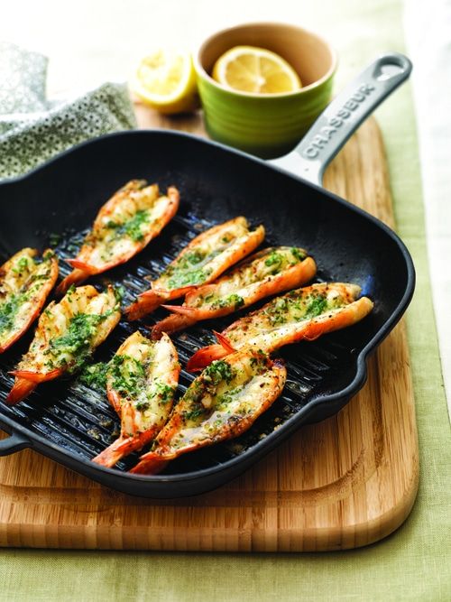 grilled lobsters with pesto and lemon on a wooden cutting board next to a bowl