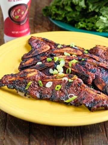 grilled meat on a yellow plate next to greens