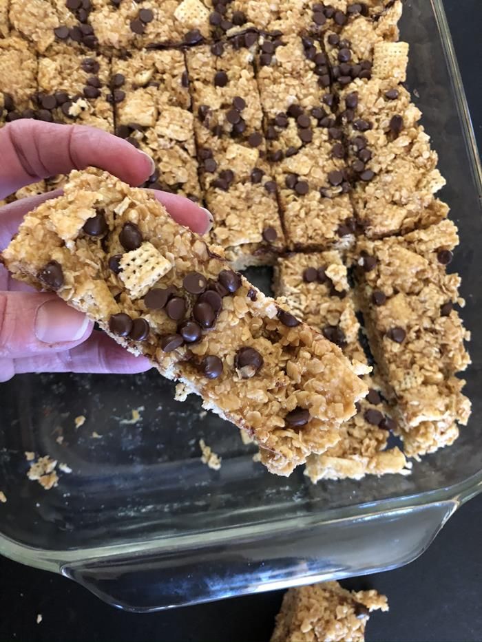 someone is holding up some granola bars with chocolate chips on top in a glass dish