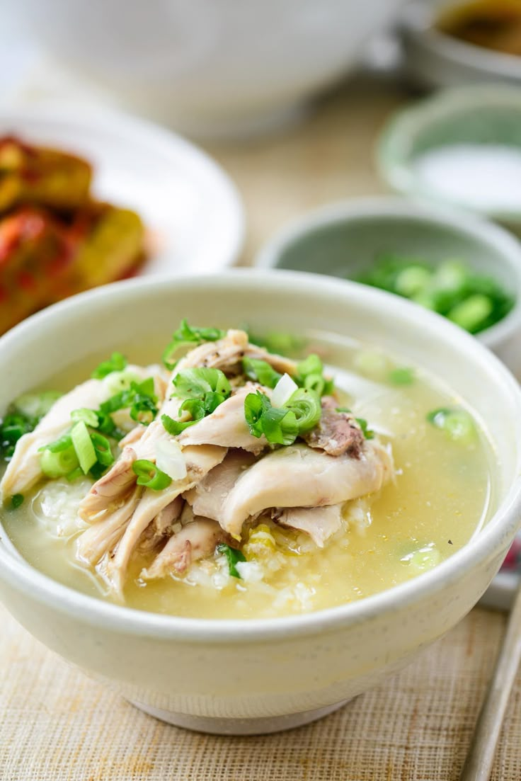 a bowl of soup with meat and vegetables in it on a table next to other bowls