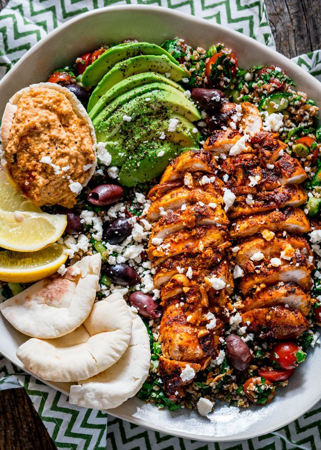 a white bowl filled with chicken, avocado, and other foods on top of a wooden table