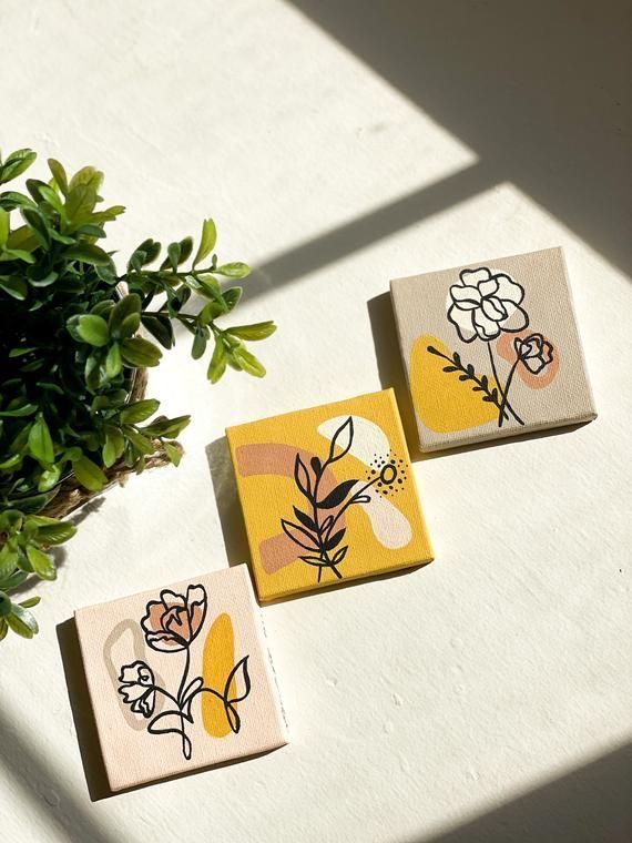 three small tiles with flowers on them sitting next to a potted plant in the sun