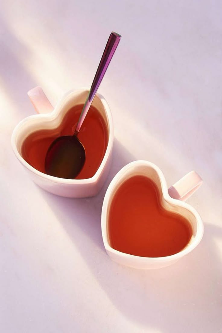 two heart shaped bowls filled with liquid on top of a white countertop next to each other