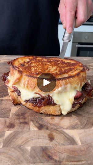 a person cutting up a sandwich on top of a wooden table with cheese and meat