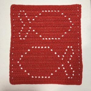 a red crocheted square with white dots on the edges, sitting on top of a table