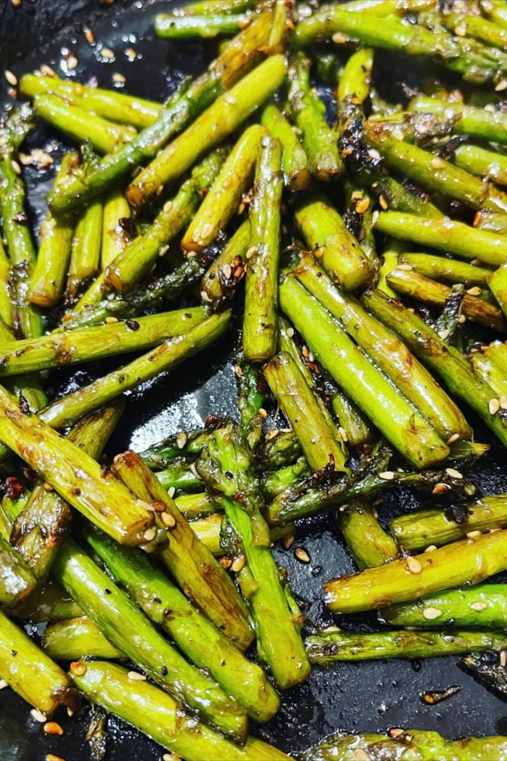 asparagus being cooked in a wok with sesame seeds and seasoning on top