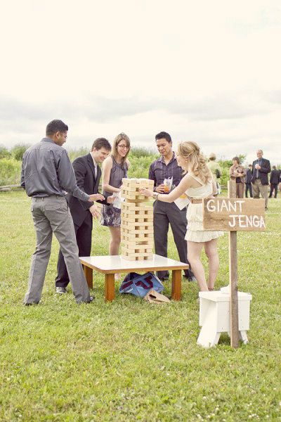 a group of people standing around a giant wooden block tower on top of a grass covered field