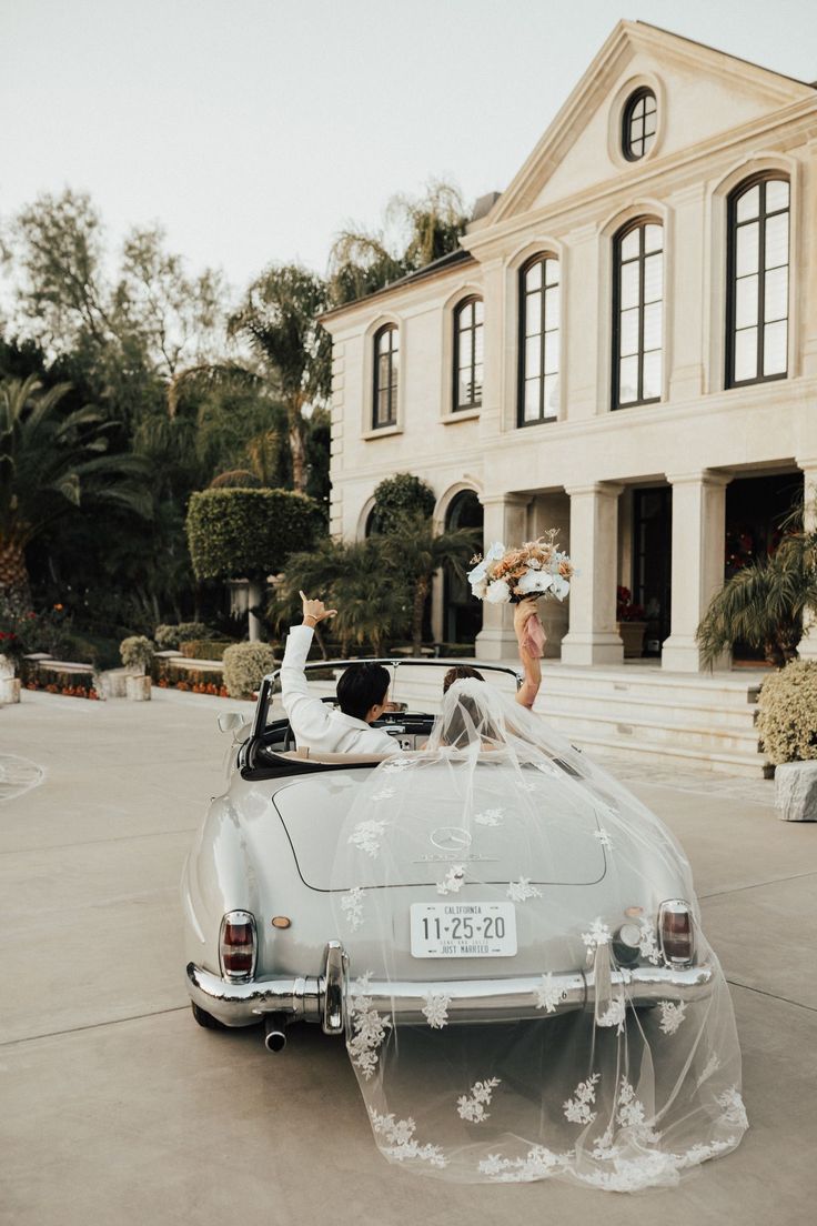 a bride and groom in an old fashioned convertible car outside a large white building with columns