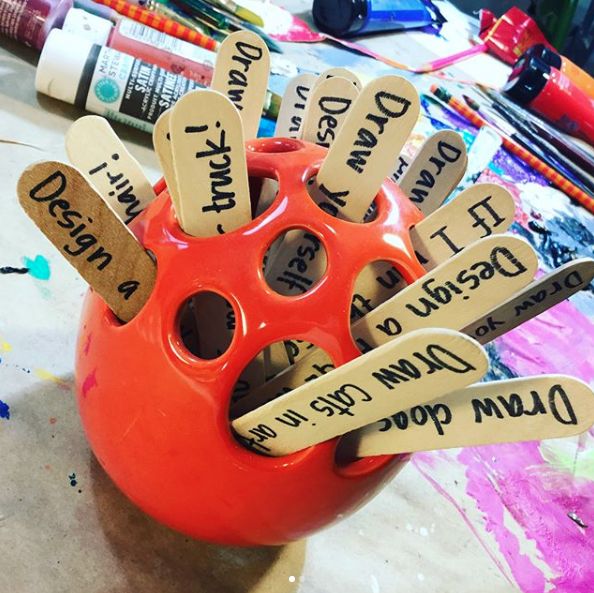 an orange vase filled with lots of writing on top of a wooden table next to crayons and markers