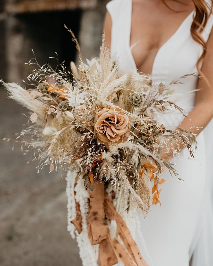 a woman in a white dress holding a bouquet with dried flowers and feathers on it